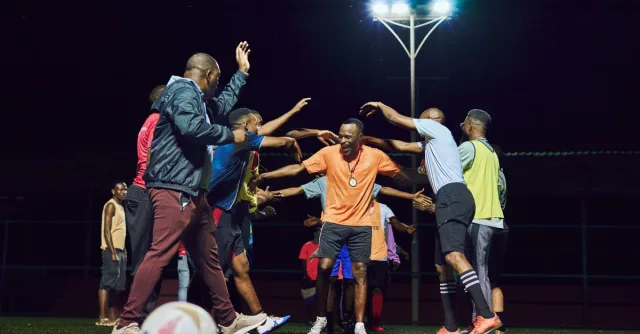 A soccer team huddles under bright stadium lights at night, fostering teamwork and unity.