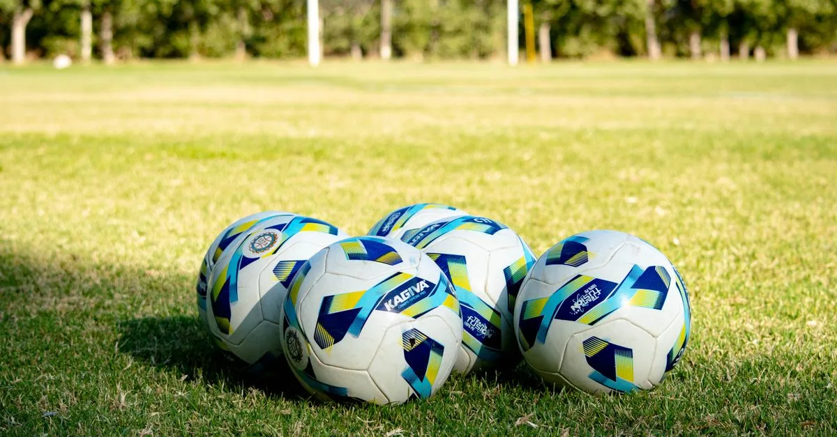 Five soccer balls rest on a green field, ready for a game in Mendoza, Argentina.