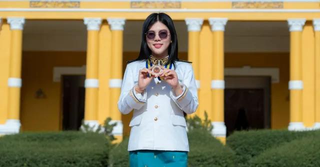 A smiling graduate holding a medal in front of a yellow building with columns.
