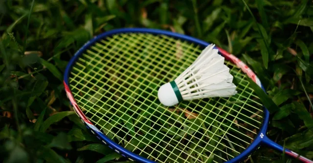 Close-up of a badminton racket and shuttlecock on grass, embodying the spirit of outdoor sports.