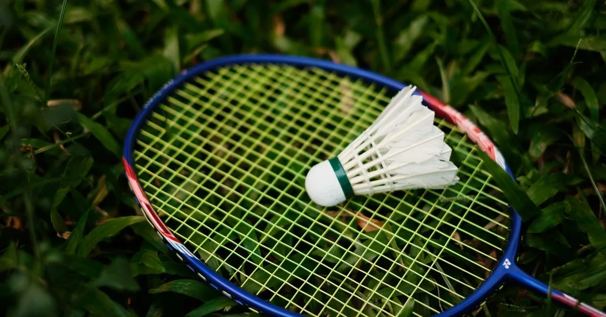 Close-up of a badminton racket and shuttlecock on grass, embodying the spirit of outdoor sports.