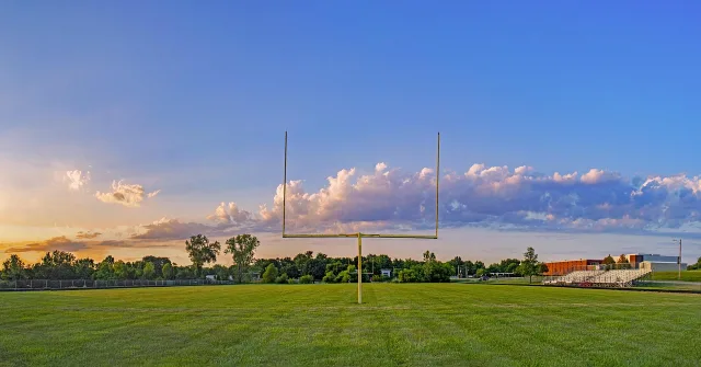A wide view of an empty American football stadium under bright stadium lights.