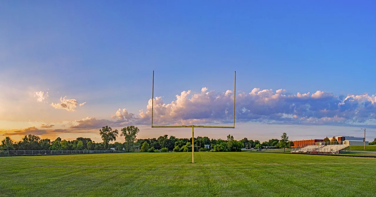 A wide view of an empty American football stadium under bright stadium lights.