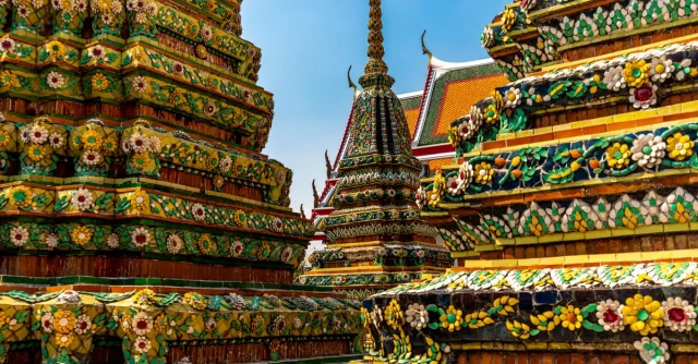 Colorful and ornate temples of Wat Pho in Bangkok, showcasing intricate Thai architecture under a clear blue sky.