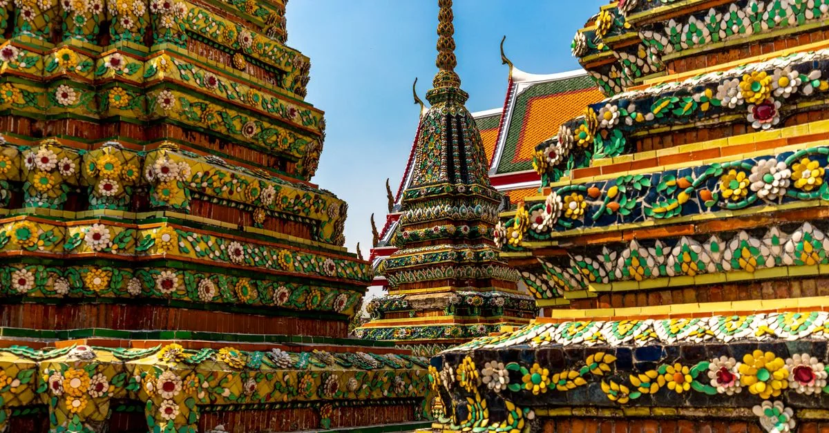 Colorful and ornate temples of Wat Pho in Bangkok, showcasing intricate Thai architecture under a clear blue sky.