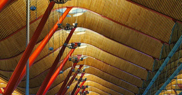 Intricate ceiling design of Madrid Barajas Airport with red poles and geometric patterns.