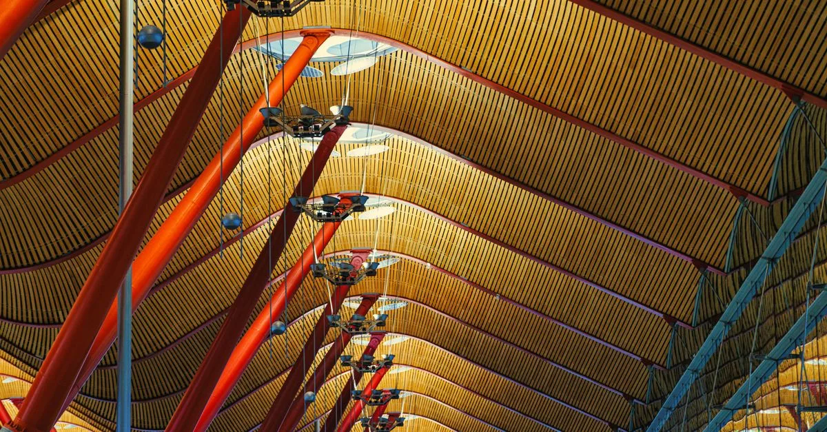 Intricate ceiling design of Madrid Barajas Airport with red poles and geometric patterns.