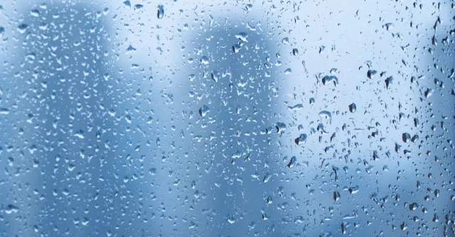Raindrops on a window with blurred cityscape background creating a tranquil mood.