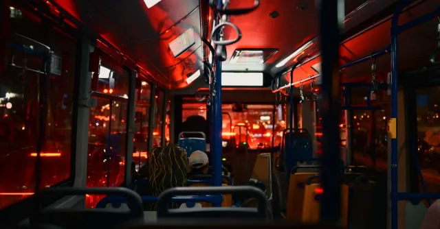 Nighttime city bus interior with passengers, illuminated by red lights, creating a moody atmosphere.