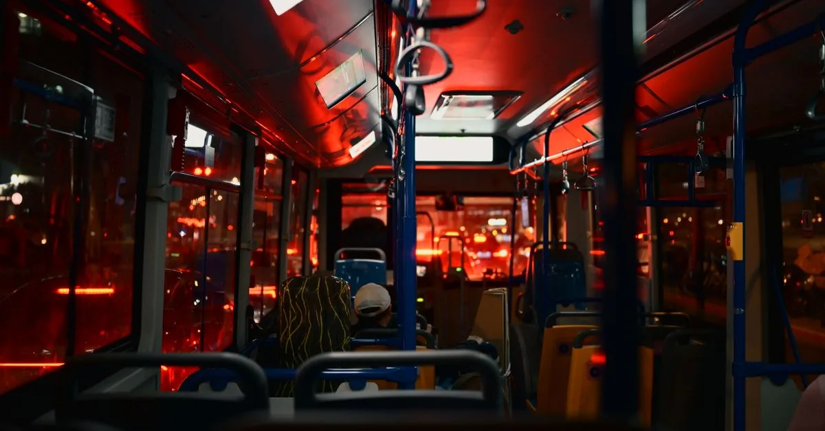 Nighttime city bus interior with passengers, illuminated by red lights, creating a moody atmosphere.