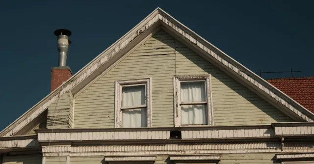 A close-up of an old wooden house facade with a chimney under a clear sky.