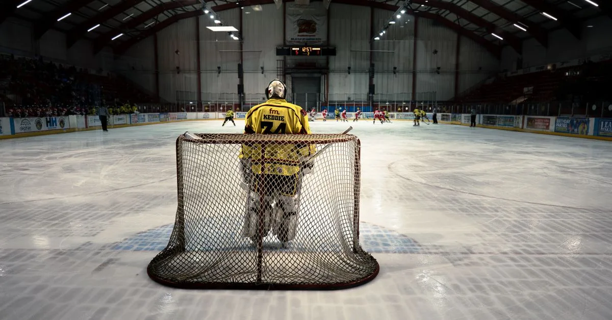 An ice hockey goalie stands in goal ready to defend during a competitive indoor match.