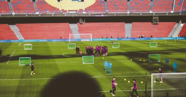 Football team training in a large empty stadium with vibrant red and blue seats.