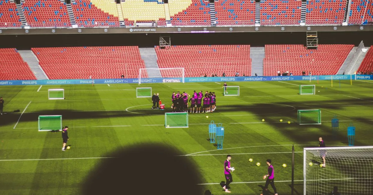 Football team training in a large empty stadium with vibrant red and blue seats.