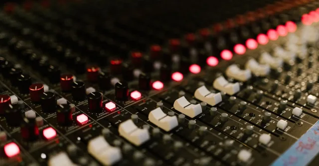 Close-up of a sound mixing console with illuminated control knobs in a music studio.