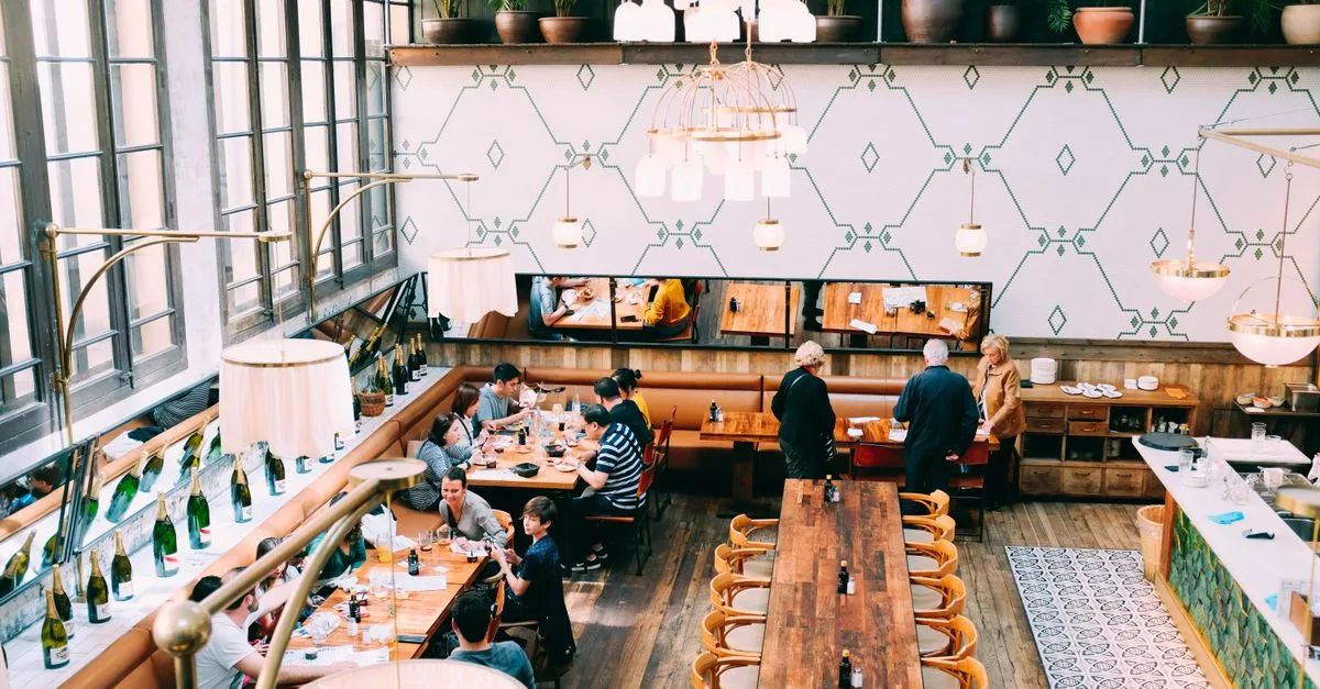 Spacious restaurant with stylish interior design, featuring wooden tables and a group of diners enjoying a meal.