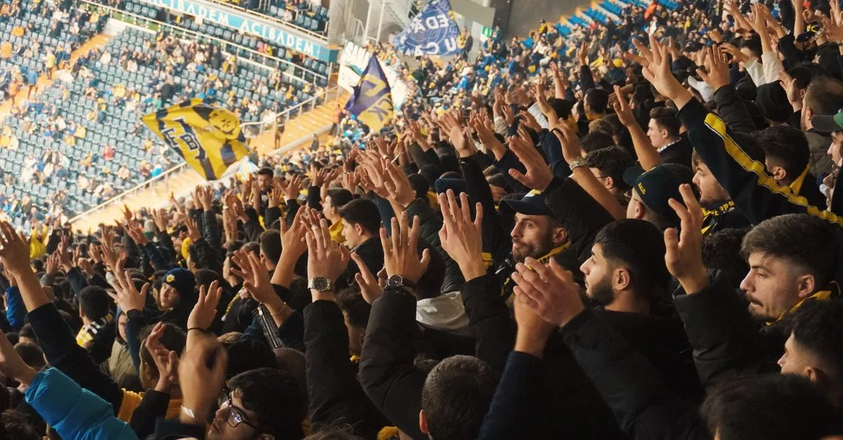 Energetic fans with raised hands in a stadium, supporting their soccer team with enthusiasm.