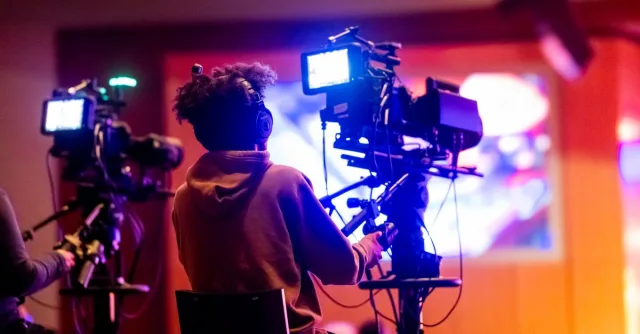 Back view of a videographer operating a camera at a live event, focusing on a vibrant indoor setup.