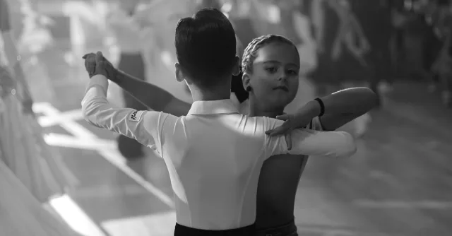 Young dancers performing ballroom dance in a black and white setting.