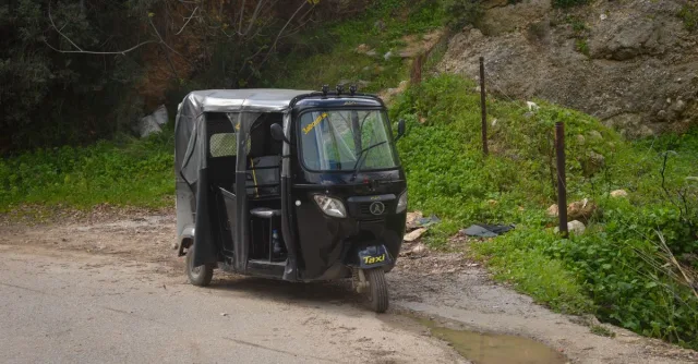 A black three-wheeler taxi parked on a rural countryside road.