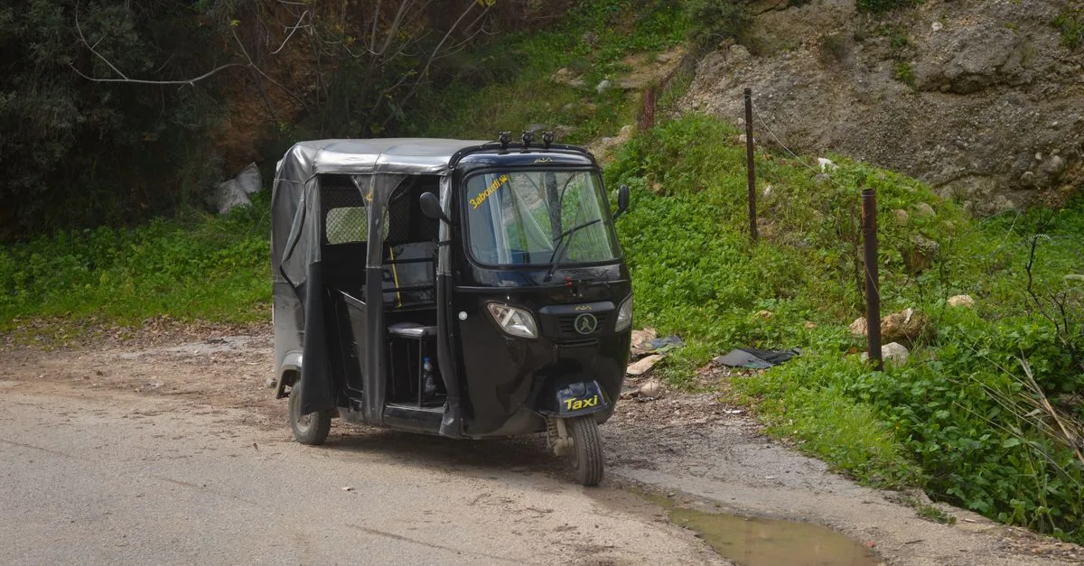 A black three-wheeler taxi parked on a rural countryside road.