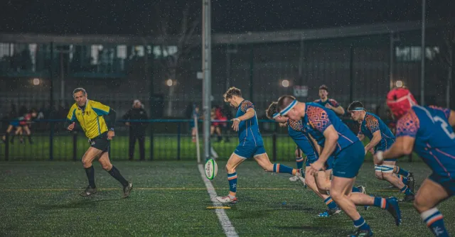 Intense night-time rugby match in England, capturing action and teamwork on a rainy field.
