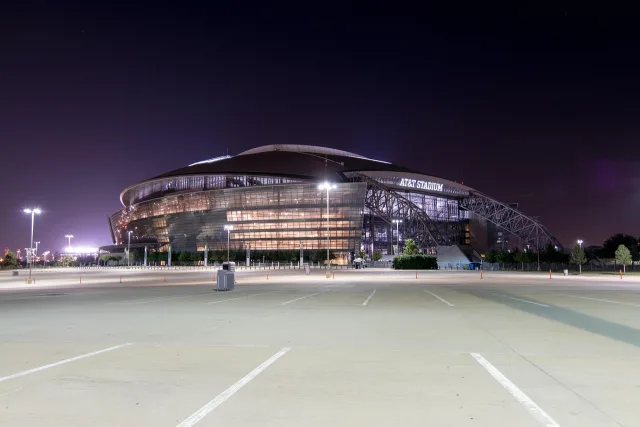 A brightly lit professional football stadium at night with an empty pitch.