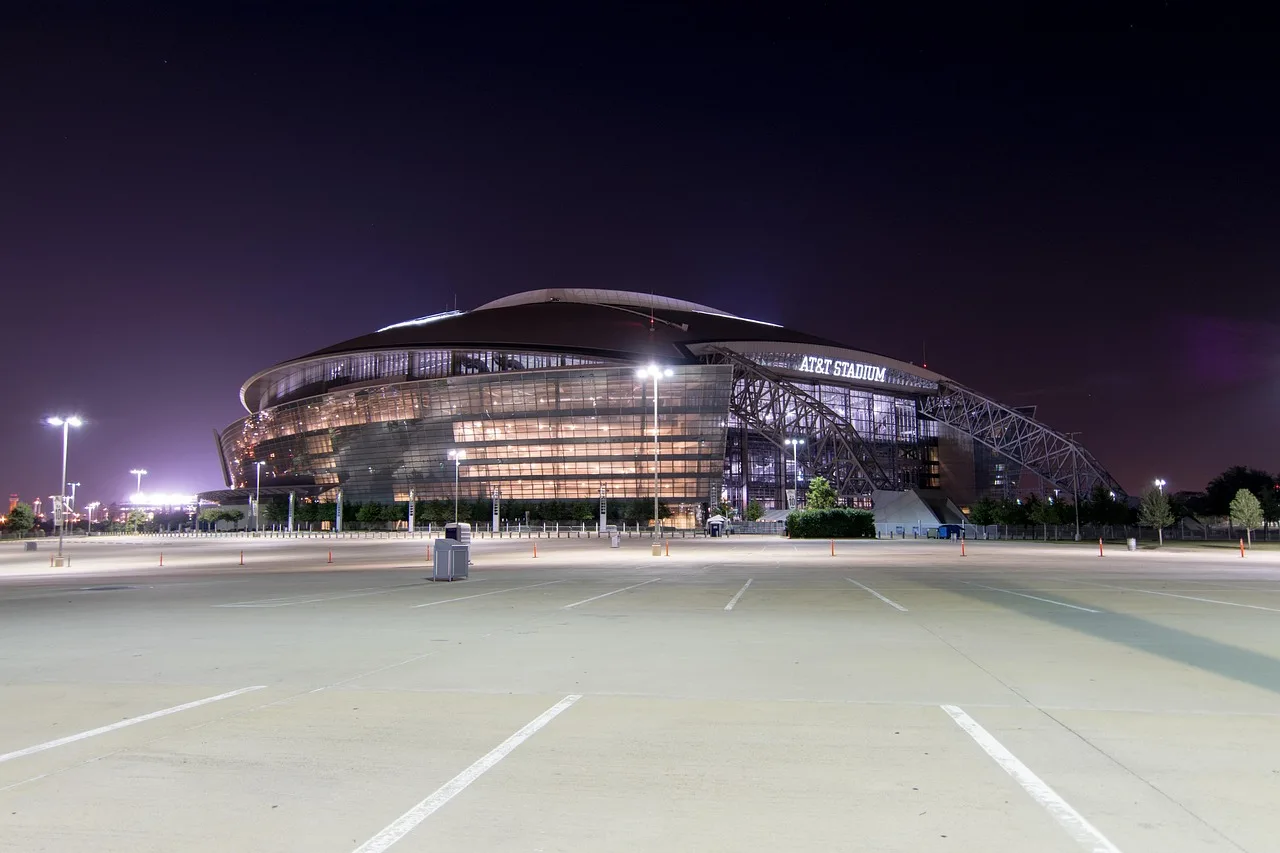 A brightly lit professional football stadium at night with an empty pitch.
