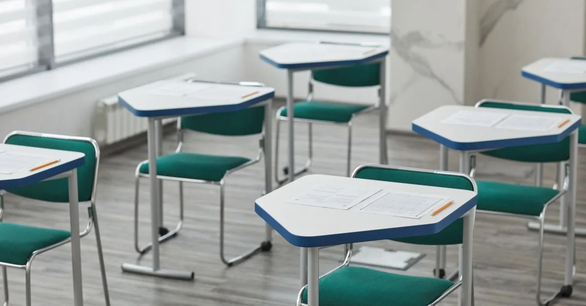 An empty classroom with arranged desks, exam papers, and pencils ready for students.