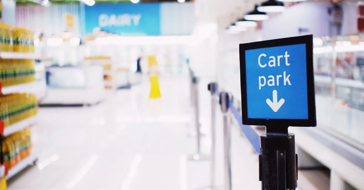 Blue signboard with inscription Cart park placed near counter with products in contemporary supermarket