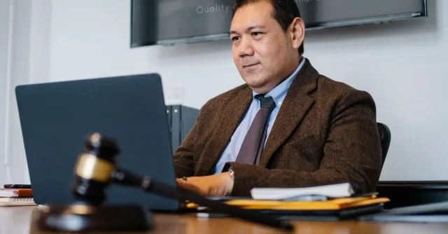 Content adult Asian male lawyer in elegant formal suit surfing contemporary netbook while working in respectable law firm