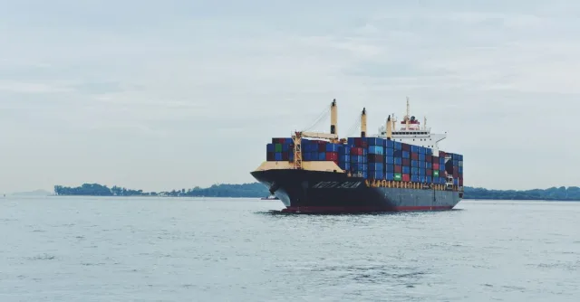 Large cargo ship transporting containers across a calm sea, symbolizing global logistics.