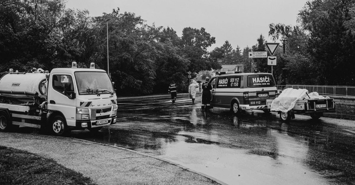 Black and white image of emergency vehicles on a rainy street with first responders.