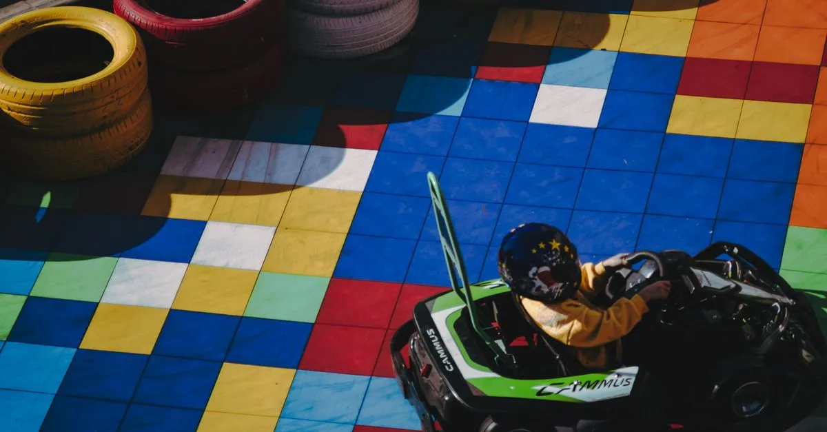 Child in go-kart racing on colorfully tiled track surrounded by tires.