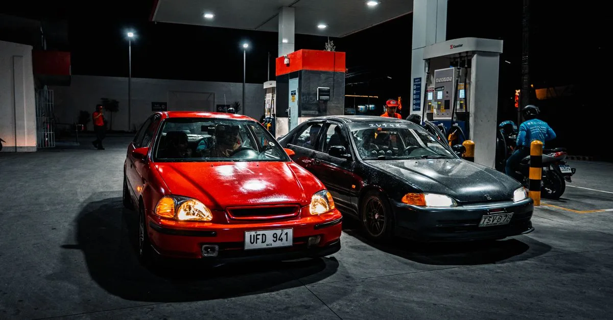 Two cars parked at a gas station at night, illuminated by overhead lights.