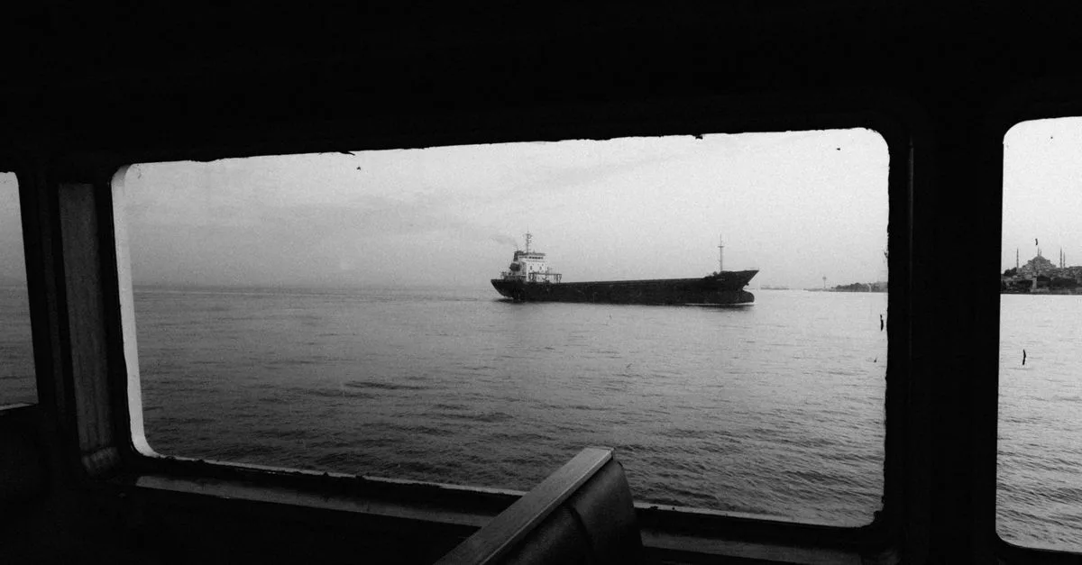 A monochrome view through a window of a container ship sailing on calm sea waters.