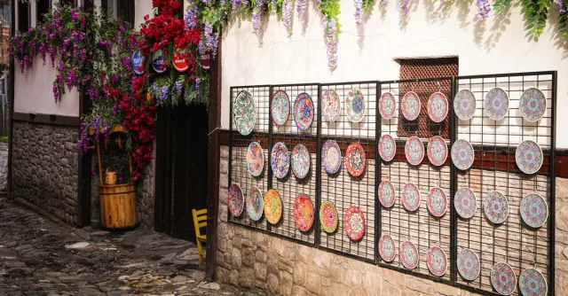 Colorful ceramic plates and vibrant flowers adorn a charming street wall.