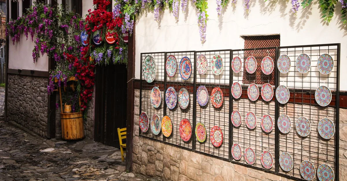 Colorful ceramic plates and vibrant flowers adorn a charming street wall.