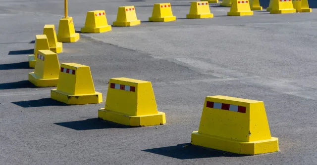 A row of bright yellow traffic barricades on a sunny asphalt road.