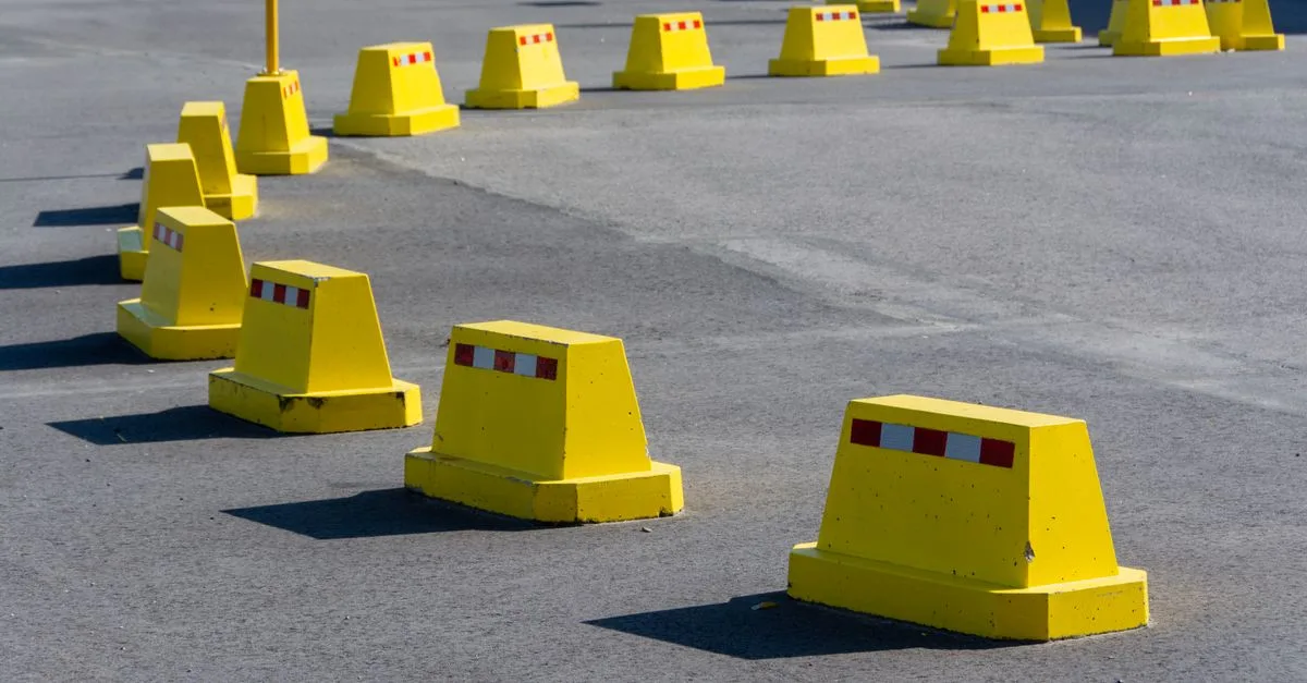 A row of bright yellow traffic barricades on a sunny asphalt road.