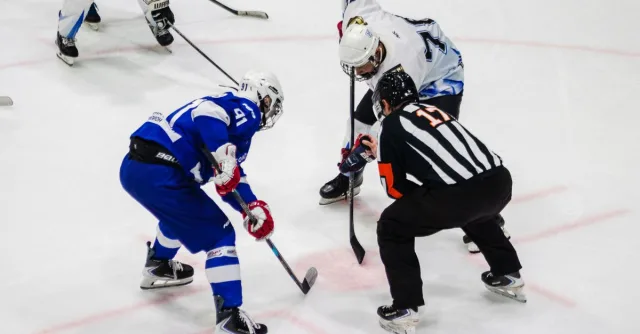 Dynamic ice hockey faceoff between two players with referee, capturing the intensity of the sport.
