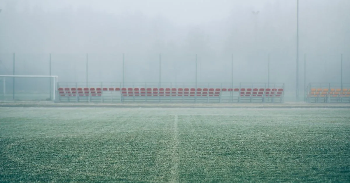 Foggy soccer field with empty bleachers, creating a serene and mysterious atmosphere.