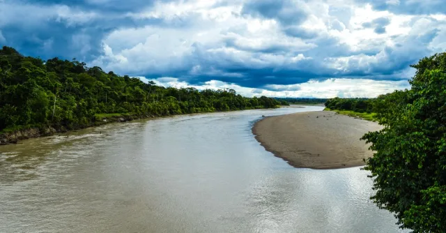 A vibrant landscape of a river winding through lush greenery under dramatic skies in Puerto Nuevo, Chocó, Colombia.