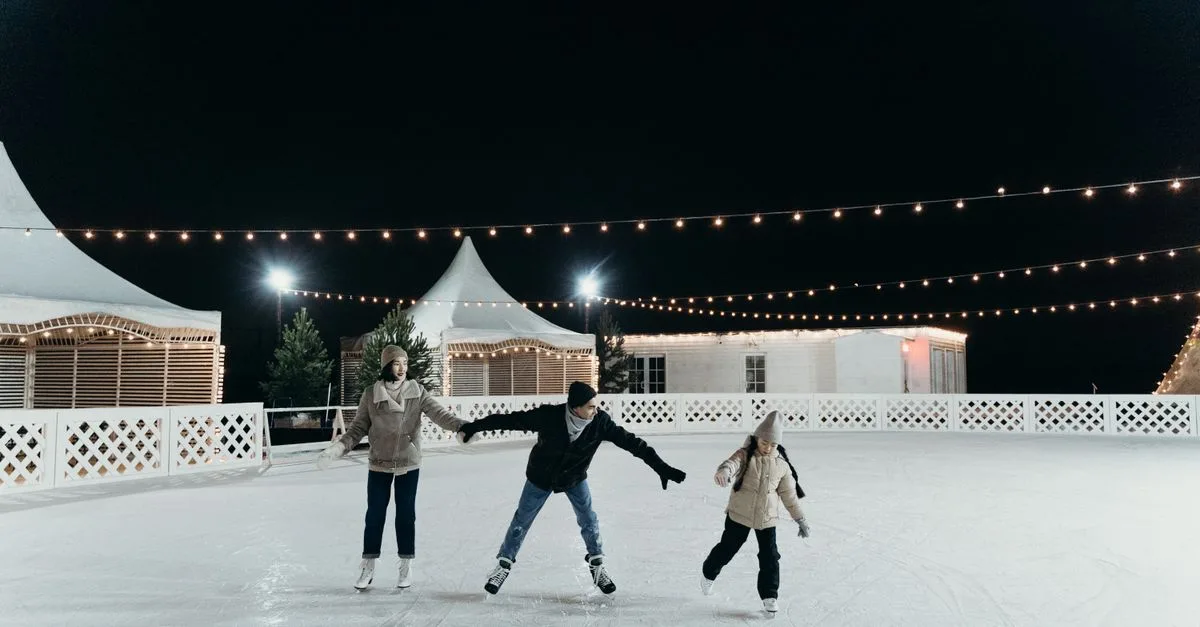A family enjoying ice skating together on an outdoor rink at night under festive string lights.