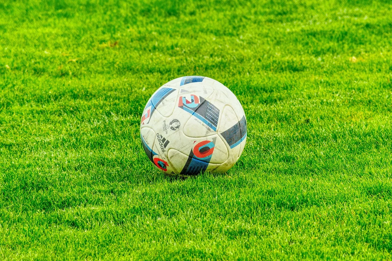 Een leeg voetbalstadion in Nederland met een strak onderhouden grasmat onder een bewolkte lucht.