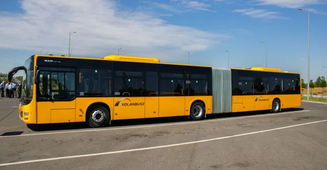 Yellow articulated city bus parked outdoors on a clear day in a spacious parking lot.