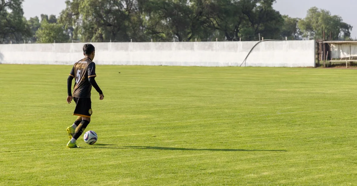 A soccer player dribbling on a lush, green field during the day.