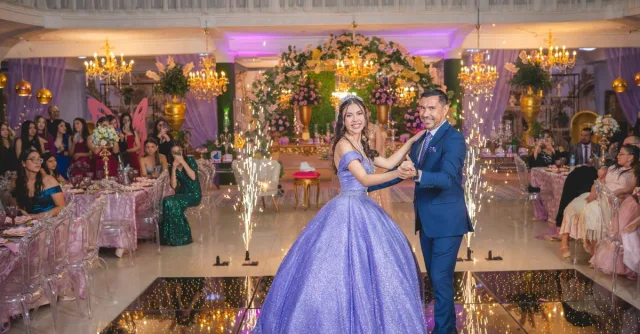 A couple elegantly dances at a lavish quinceañera celebration amidst joyful guests and sparkling decor.