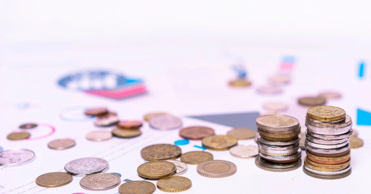 Stack of assorted coins with financial documents on a white background, highlighting the concept of savings.