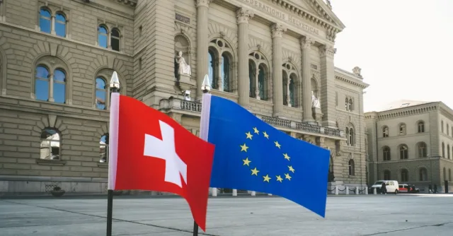 Front view of Swiss Parliament Building in Bern with Swiss and EU flags.
